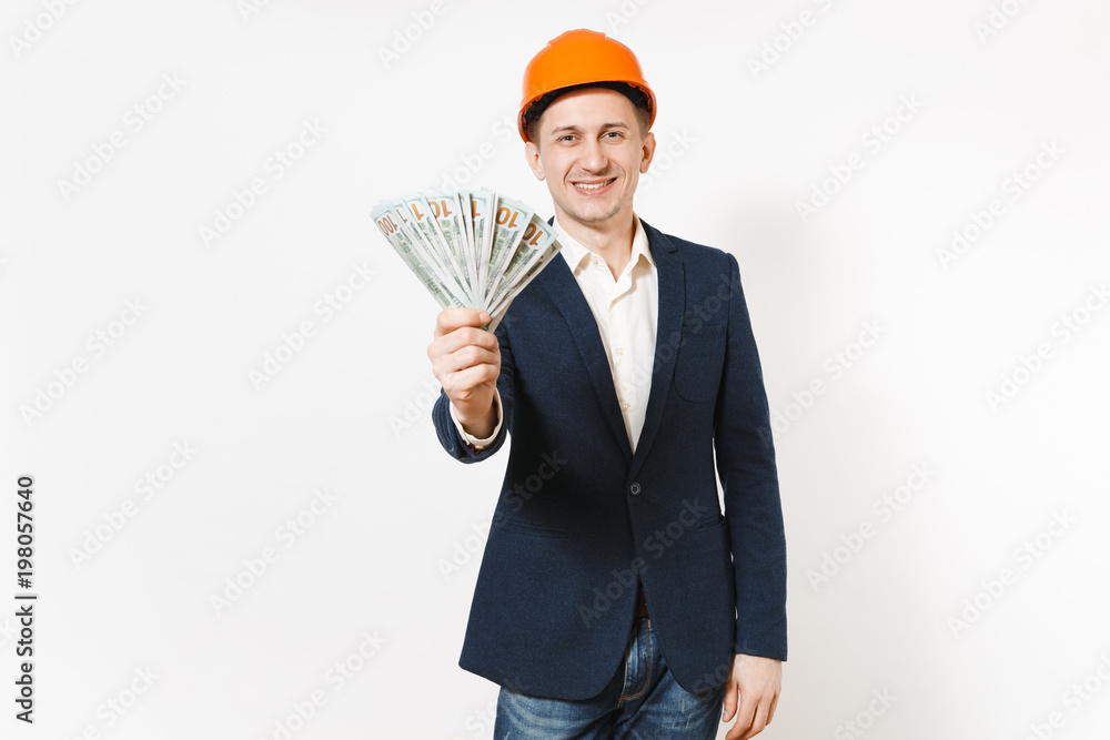 Smiling businessman in dark suit, protective hardhat holding bundle of dollars, cash money and pointing index finger up on copy space isolated on white background. Male worker for advertisement. Smiling businessman in dark suit, protective hardhat holding bundle of dollars, cash money and pointing index finger up on copy space isolated on white background. Male worker for advertisement.
