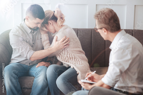 Feeling desperate. Sad unhappy blonde woman leaning on her husbands shoulder and crying while having lots of problems