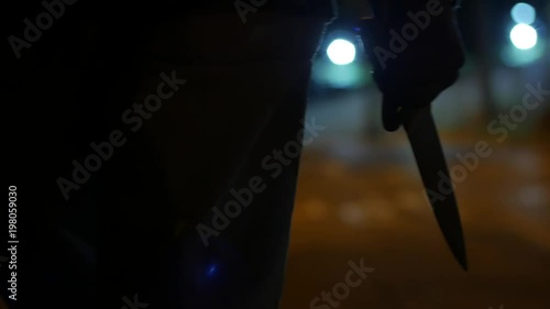 A MAN WALKS AT NIGHT HOLDING A BIG KNIFE