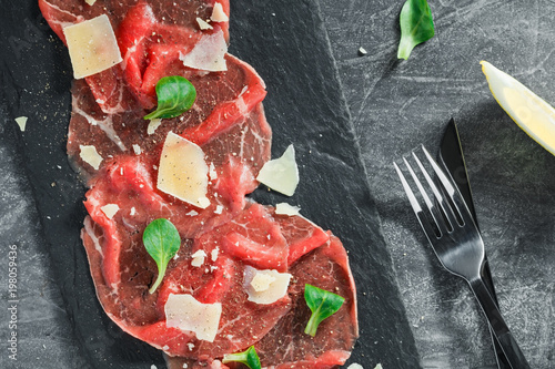 Photos Top view of the raw beef carpaccio with parmesan cheese on a black shale service board