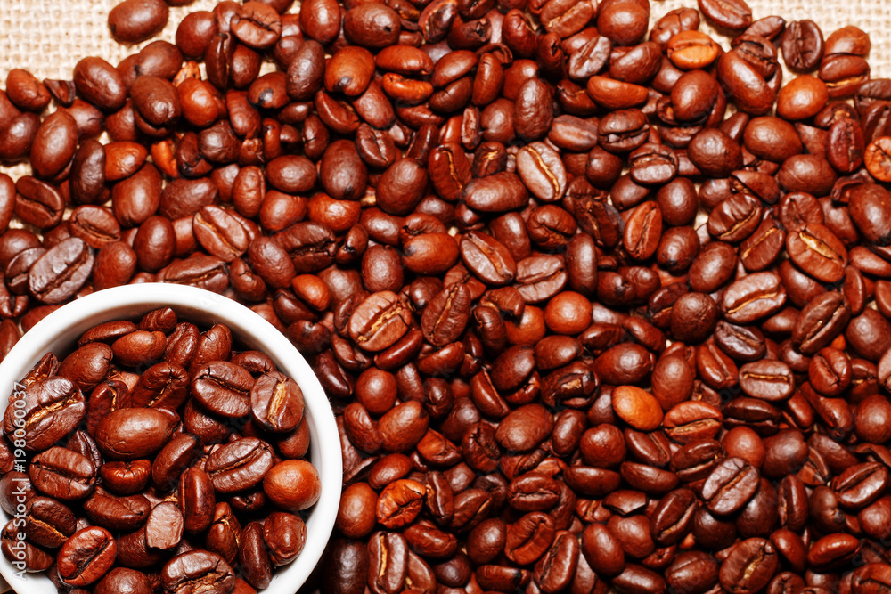 Fototapeta premium White cup and coffee beans on the background of sacking. view from above