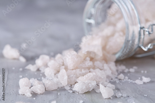 Spa concept. Bath salt pouring out of glass jar on texrured background, close-up, selective focus