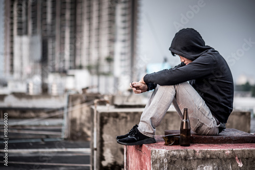 Mystery man in hoody jacket, sitting and hugs his knees up with an empty and broken bottle. depression self destruction suicidal addicts drug, Major depressive disorder concept photo