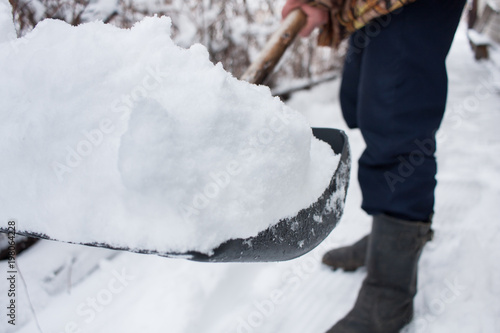 close up view of snow shovel with snow in man's hands. Man clean backyard of his house after blizzard. Spring snow cleaning.