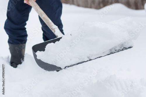 close up view of snow shovel with snow in man's hands. Man clean backyard of his house after blizzard. Spring snow cleaning.