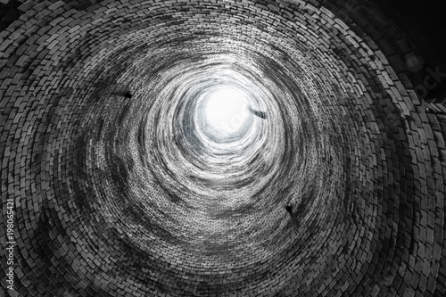 Abstract image looking up an abandoned brick smoke stack. Round circle repeating pattern of old bricks, and light at the end