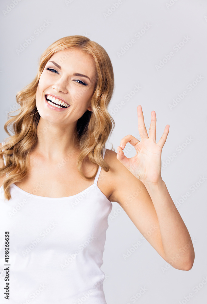 Fototapeta premium Young woman showing okay gesture, over grey