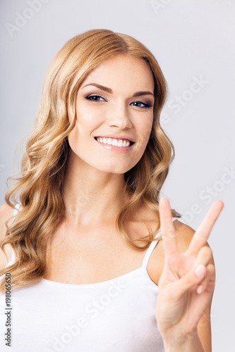 Woman showing two fingers or victory gesture, on grey