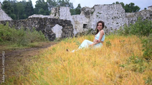 Girl sitting in a clearing on the background of an old fortress photo