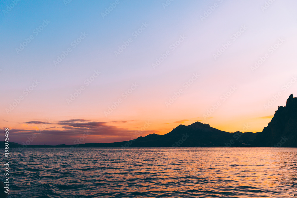 Beautiful red and purple sunset at Black sea with silhouette of rocks Karadag, Crimea.