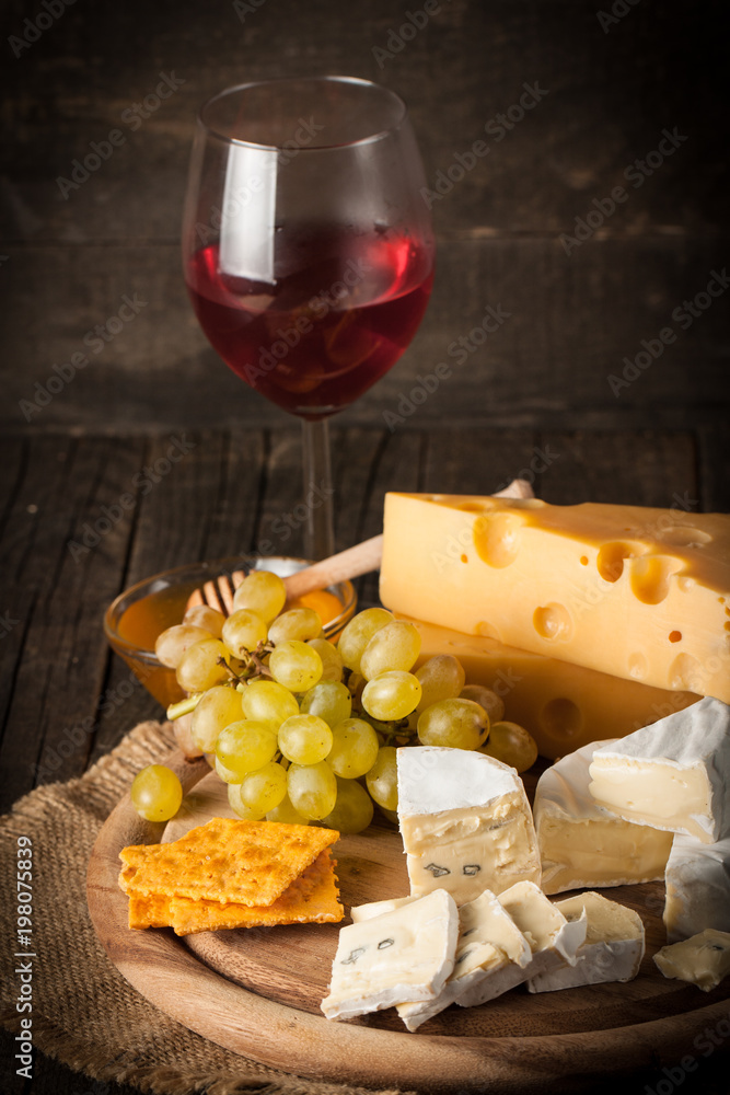 Slate board with various cheese and a glass of red rose wine. Brie. Camembert. Gouda, Masdaam, Roquefort, Cheddar and grapes on a wood with nuts, honey, crackers, blue cheese. Italian, French cheese.