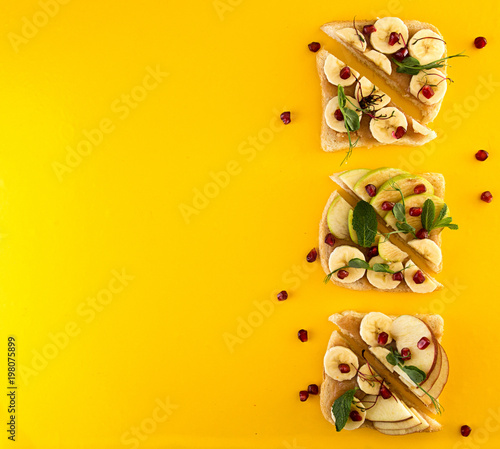 Healthy breakfast sweet toasts with apple, banana, pomegranate and caramel on yellow background. Clean eating healthy vegetarian food concept. Top view.