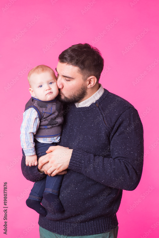 Happy father holding baby son in hands over pink background