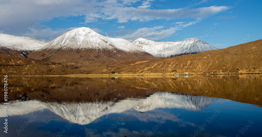 Snow covered peaks of a mountain range and its reflections in Loch Ainort on the Isle of Skye in the Scottish Highlands