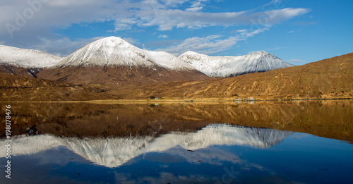 Snow covered peaks of a mountain range and its reflections in Loch Ainort on the Isle of Skye in the Scottish Highlands