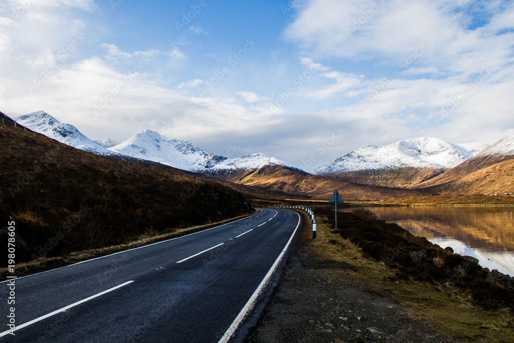 Road winding through the mountains of the southern Isle of Skye, Scotland, with snow covered peaks in the background