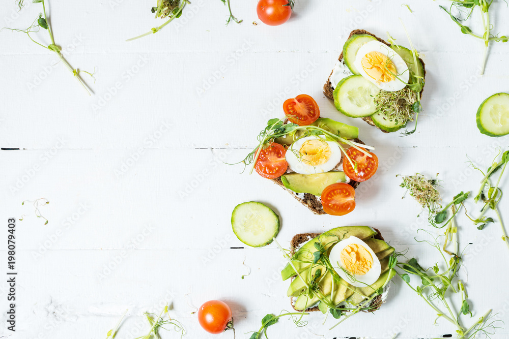 Tasty sandwiches with egg, avocado and vegetables on wooden white rustic background. Tasty sandwiches with egg, avocado and vegetables on wooden white rustic background.