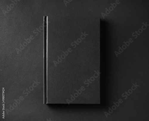 Photo of blank black book cover on black paper background. Flat lay.