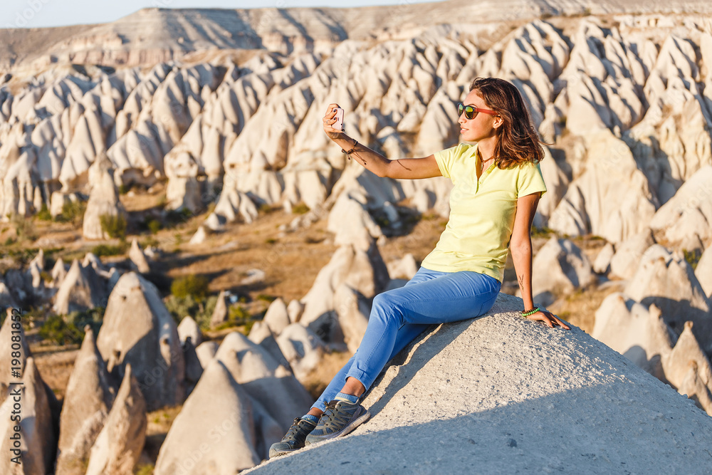 smiling woman in sunglasses taking selfie photo on a smartphone in Cappadocia, Turkey
