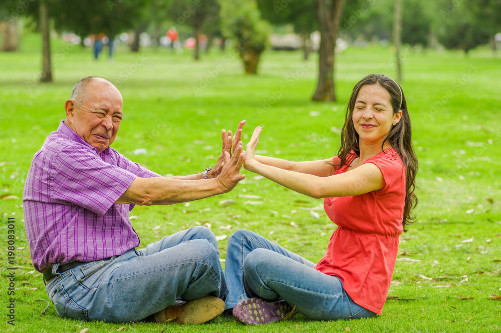 Fototapeta premium Outdoor view of father and daughter rejecting each other at outdoors sitting in the grass, in the park