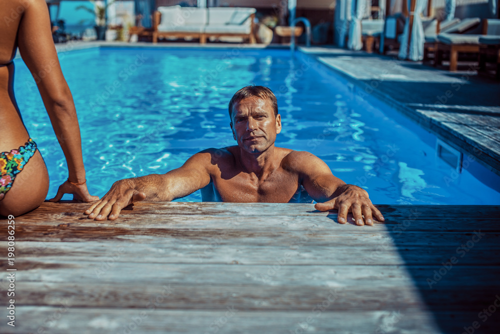 Fototapeta premium An attractive couple, handsome muscular male and sexy woman sitting near the pool and enjoying a vacation.
