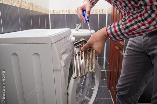 Obraz na plátně a young repairman with a screwdriver repairs an old heating element or a teng from a faulty washing machine