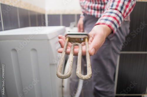 the repairman is holding a defective dirty heating element or a tan close-up from a washing machine photo