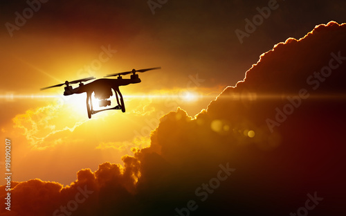 Silhouette of flying drone in glowing red sunset sky photo