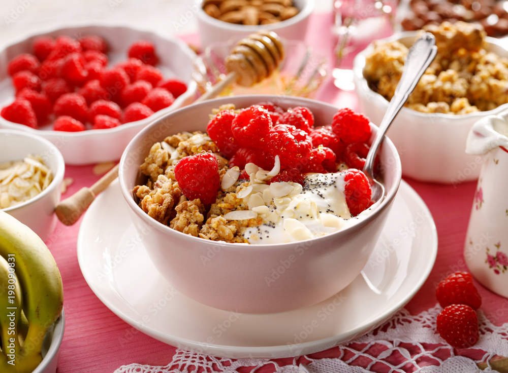 Granola with natural yogurt, raspberries, honey, almond flakes, and poppy seeds in a bowl on a pink wooden table. A delicious and nutritious breakfast or dessert. Healthy eating concept Granola with natural yogurt, raspberries, honey, almond flakes, and poppy seeds in a bowl on a pink wooden table. A delicious and nutritious breakfast or dessert. Healthy eating concept