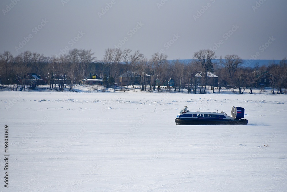 Hovercraft is rushing through a river covered with ice on a clear winter day Hovercraft is rushing through a river covered with ice on a clear winter day