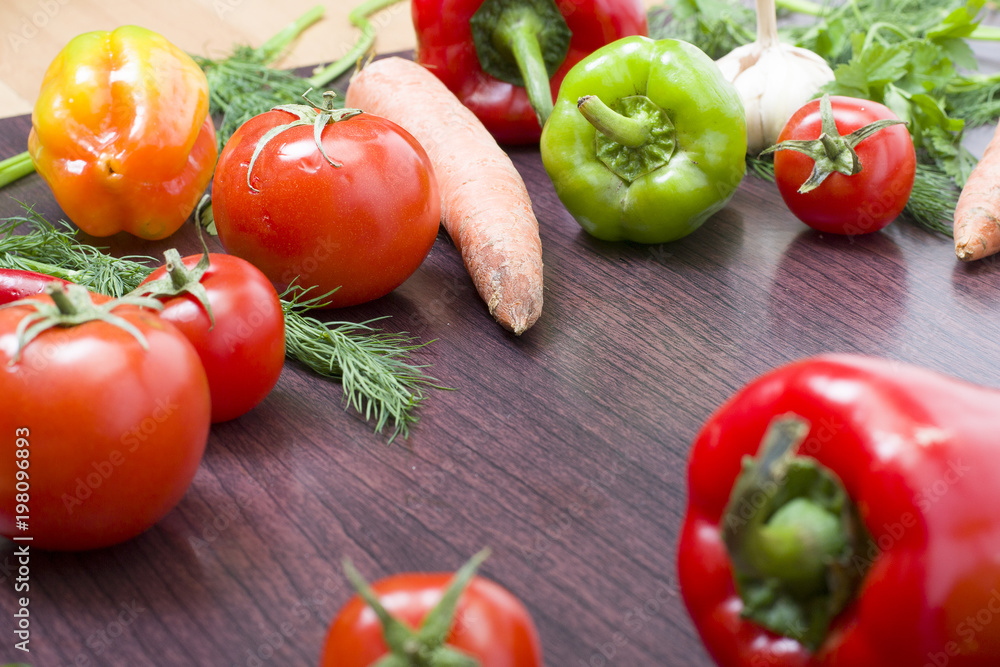 Red tomatoes and green peppers on a table on the background of vegetables. Fresh tomatoes and peppers on a wooden brown table.. Red tomatoes and green peppers on a table on the background of vegetables. Fresh tomatoes and peppers on a wooden brown table..