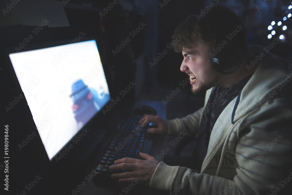 Portrait of an evil gamer while gaming at home behind a computer. An emotional man plays computer games and gets angry. Gamer concept.