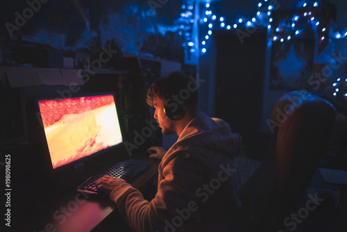 A focused gamer sits at the computer at home in the cozy room and plays horror games on the computer. A man sits at the computer at night and looks at the monitor