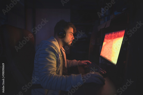 A cute male gamer sits in a cozy room behind a computer and plays games. Gamer plays horror game at night. Computer games. Gamer concept.