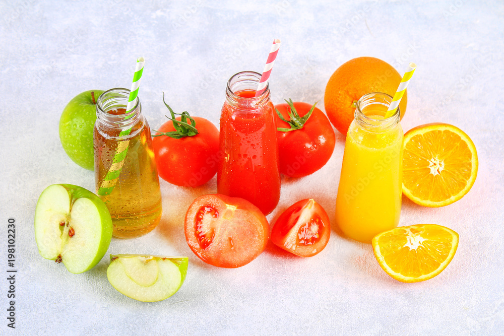 Bottles with fresh orange, apple, tomato juice and colored tubules on a gray concrete table. Bottles with fresh orange, apple, tomato juice and colored tubules on a gray concrete table.