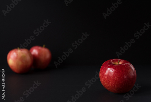 A shiny red apple isolated on black background. Two other apples out of focus in background