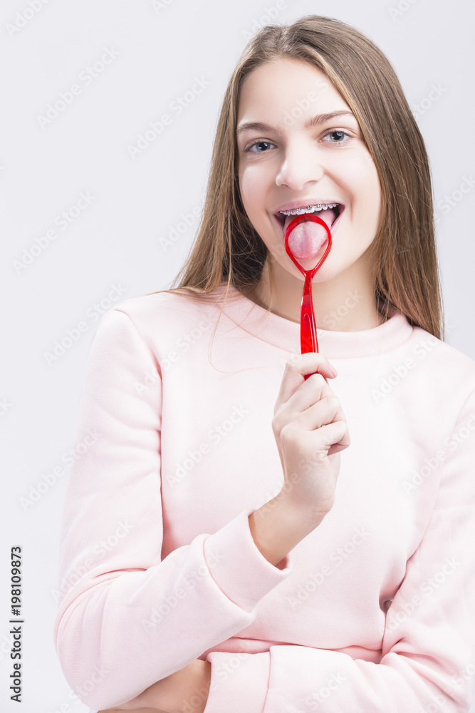 Dental Health Concepts. Caucasian Teenage Girl with Correcting Teeth Brackets. Posing with Special Tongue Cleaning Scraper. Dental Health Concepts. Caucasian Teenage Girl with Correcting Teeth Brackets. Posing with Special Tongue Cleaning Scraper.