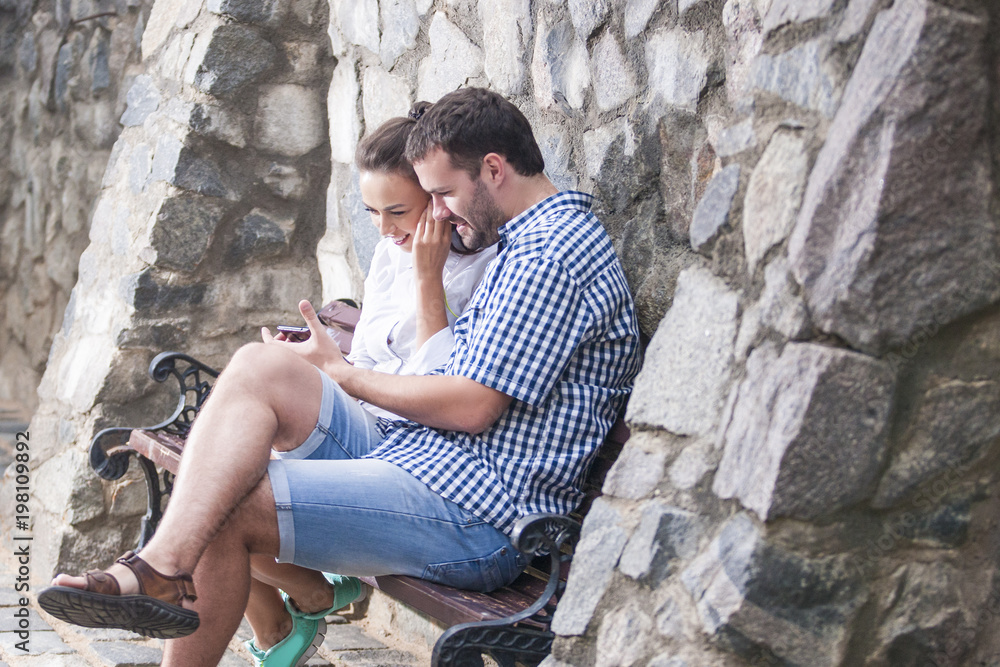 Love,Relationships, Communication Concepts. Happy and Positive Caucasian Couple Sitting Together with Smartphone and Listening to Music in Headphones.