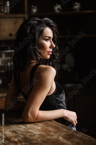 Beautiful brunette in the kitchen, modern housewife, fashion, wooden brown furniture, dressed in blue jeans and a blue shirt © boykovi1991