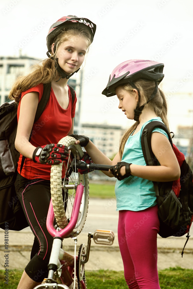 Obraz premium Bicycle tire pumping and repair by child bicyclist. Girl repairing bicycle on road . Kids pump up tire. Children return home from school on bicycles. Tone image. They help children repair bicycles.
