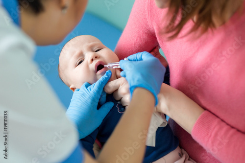 Baby on mothers hand at hospital. Nurse making infant oral vaccination against rotavirus infection. Children health care and disease prevention