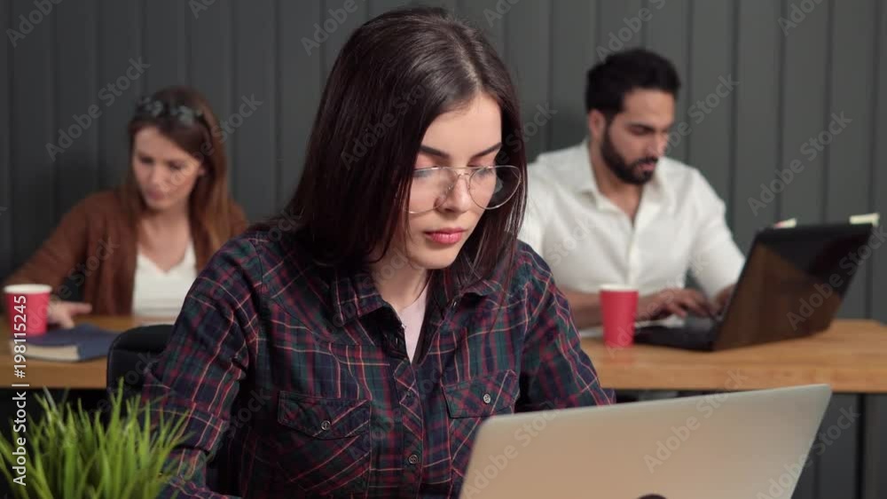 Busy brunette using silver computer, talking to bearded male colleague in smart white shirt, indoor shot of working atmosphere Busy brunette using silver computer, talking to bearded male colleague in smart white shirt, indoor shot of working atmosphere