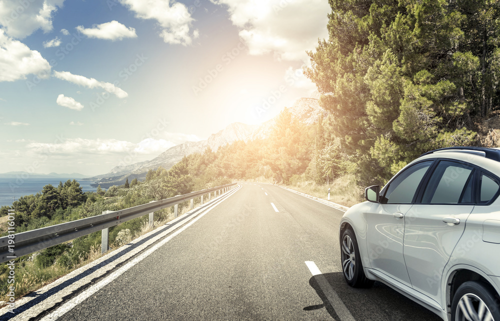 Naklejka premium Biały samochód pędzący wzdłuż szybkiej autostrady w słońcu.