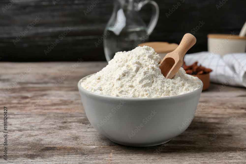 Bowl and scoop with flour on wooden table Bowl and scoop with flour on wooden table