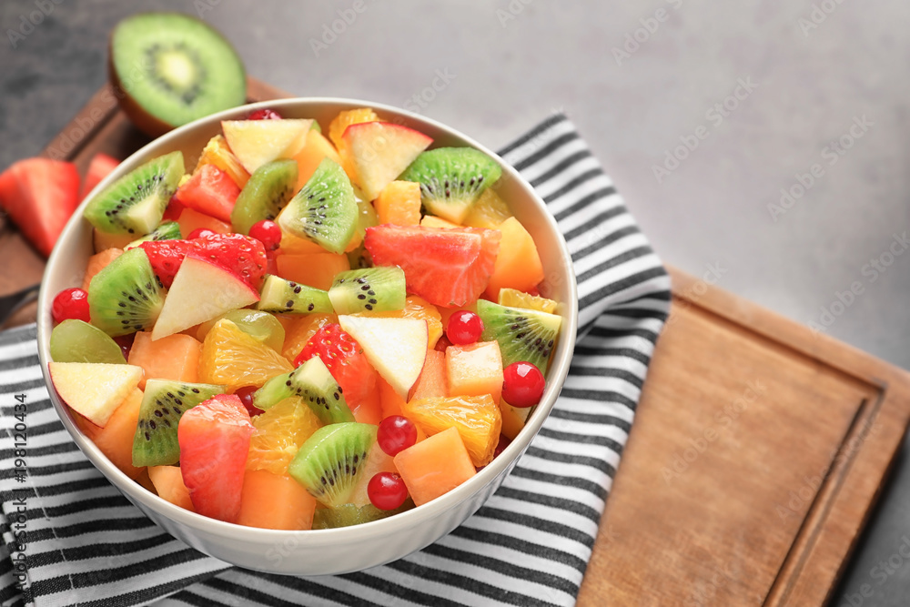 Bowl with fresh cut fruits on wooden board
