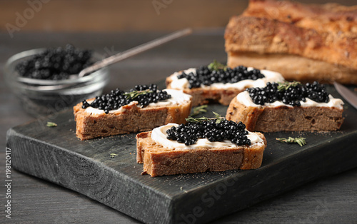 Sandwiches with black caviar and butter on wooden board