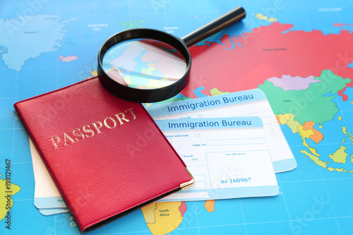 Slika na platnu Magnifying glass and passport with arrival cards of immigration bureau on world