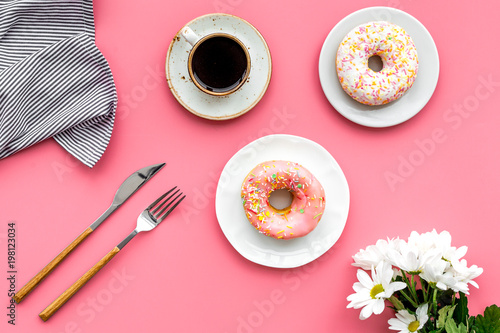 woman desk with flowers, coffee and donuts for breakfast in spring desing pink background flat lay photo