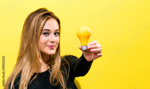 Young woman holding a light bulb on a yellow background