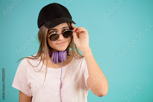 young female with sunglasses and headphones is wearing black cap isolated on the blue background. sportswoman photo